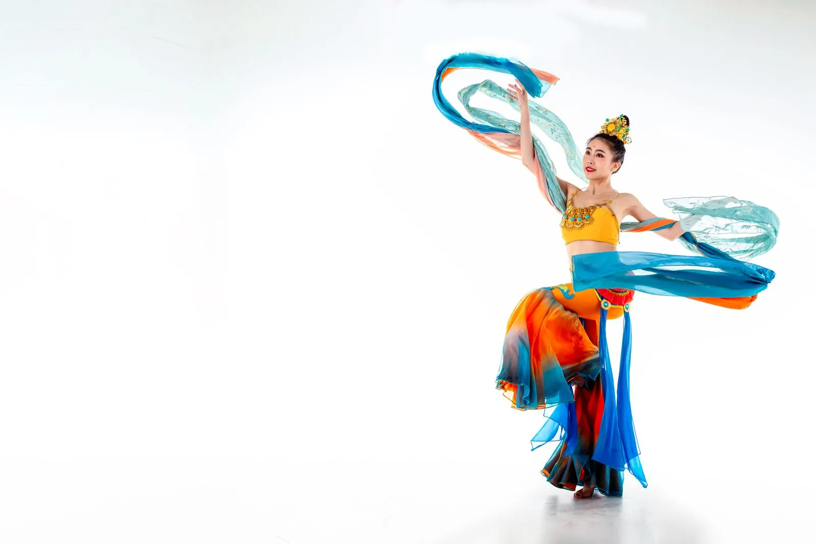 A graceful dancer performing in colorful traditional attire against a white background, showcasing elegance and fluidity.